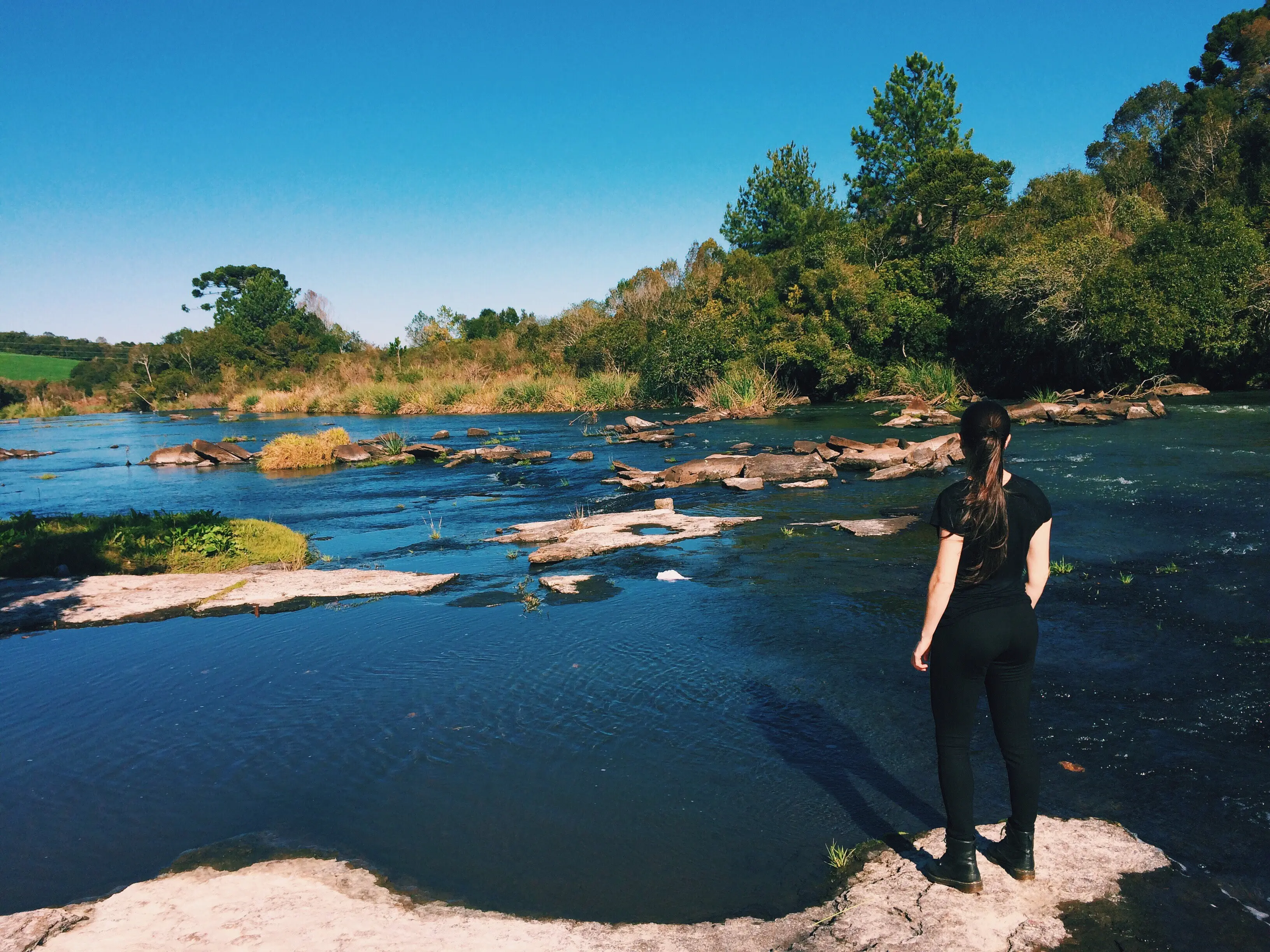 Rückansicht einer Frau, die an einem See in einem Wald steht.